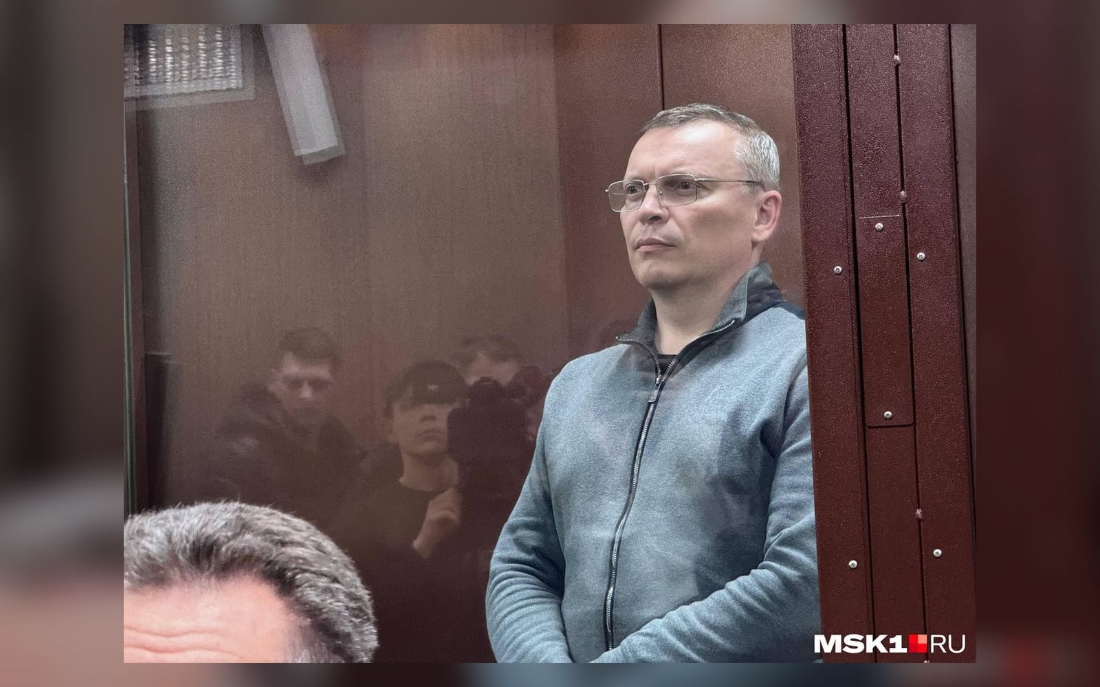 Андрей Фалейчик в зале суда — портретный кадр в стеклянном боксе. Не момент задержания.